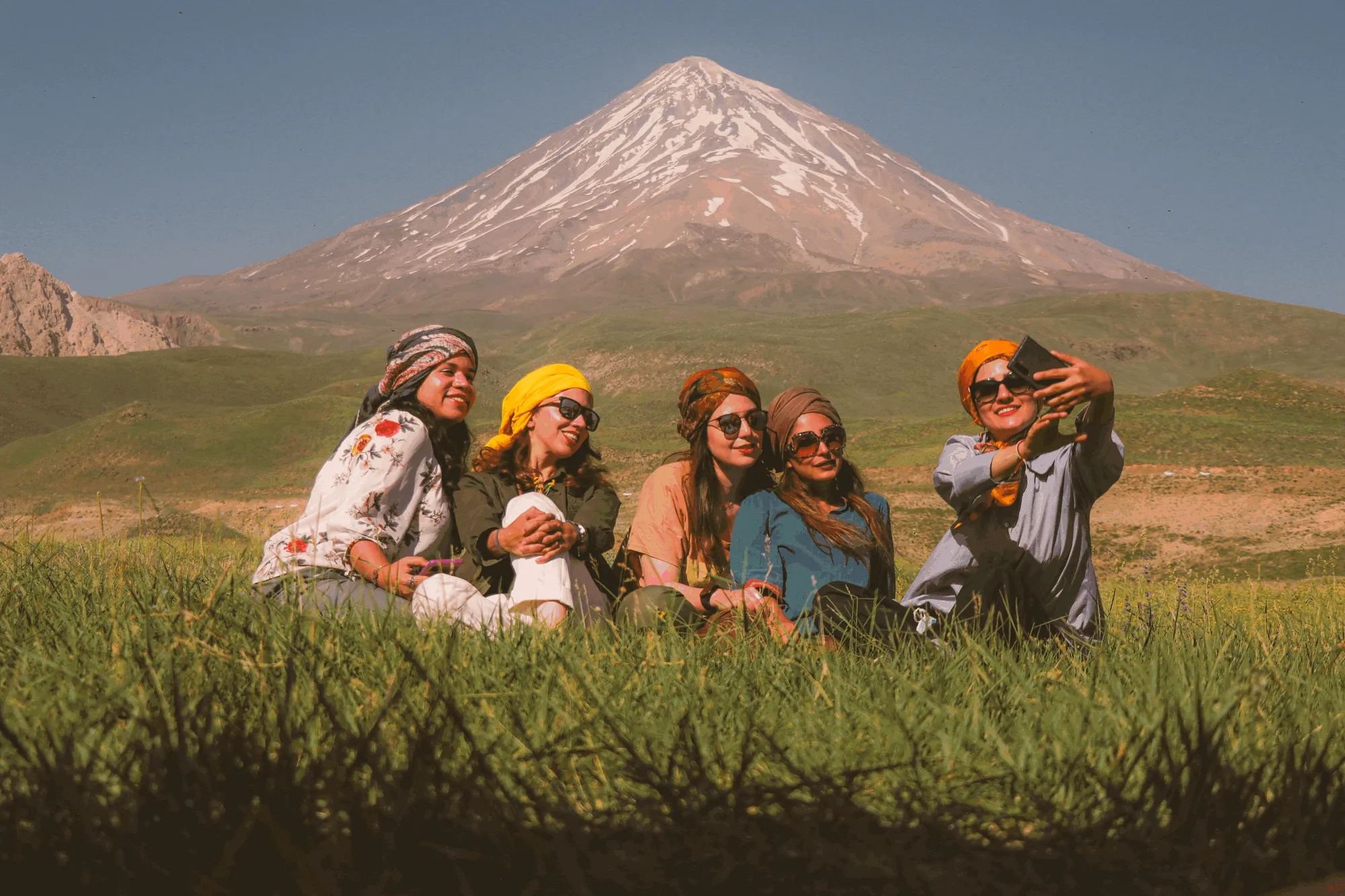Group of women friends taking a selfie together in front of a snow-capped mountain