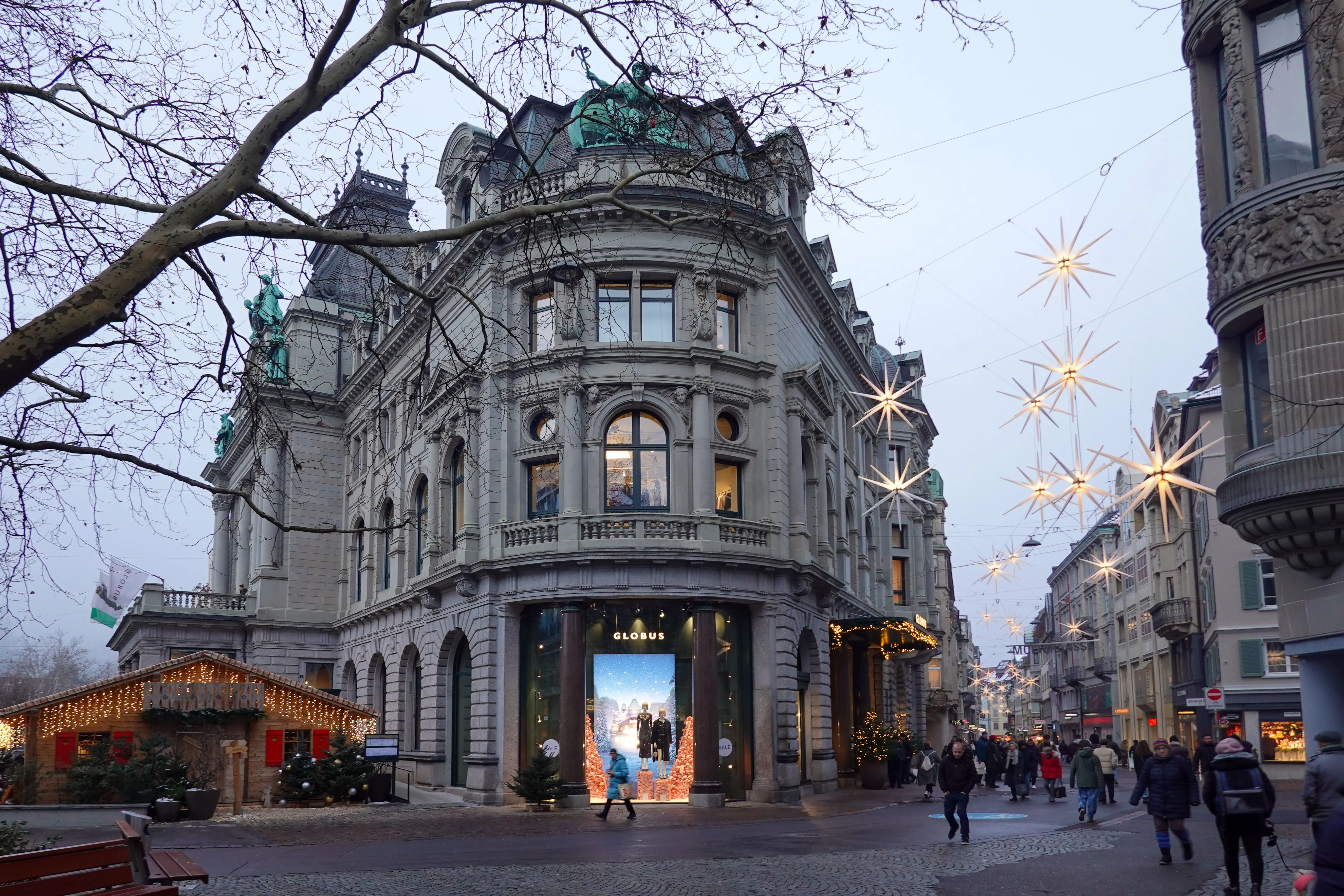 Zurich's Bahnhofstrasse at dusk in December, the Globus department store lit for Christmas with market stalls and star lights
